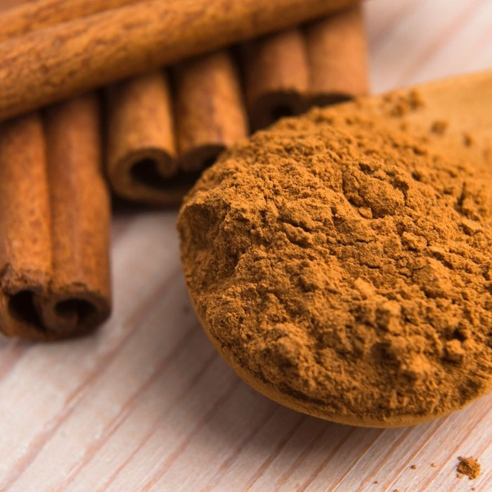 Ground cinnamon on wooden spoon with cinnamon sticks nearby.