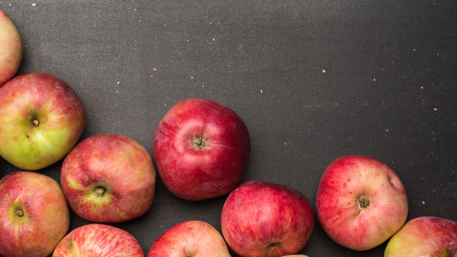 Group of red and green apples on black textured background.