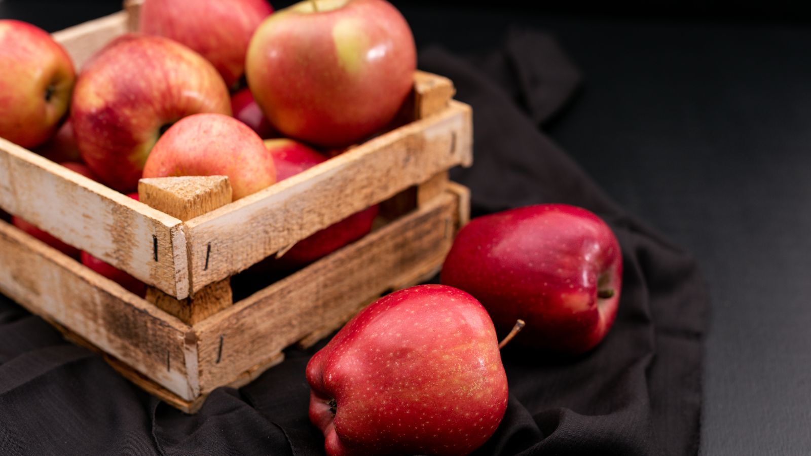 Fresh red apples in a rustic wooden crate on black cloth.