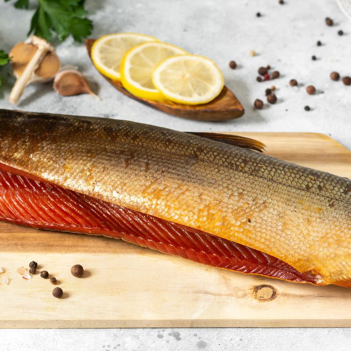 Smoked salmon fillet on cutting board with spices and herbs.