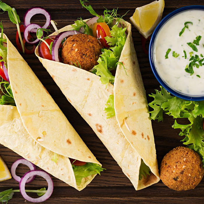 Tortilla wraps with fresh vegetables and yogurt sauce on wooden board