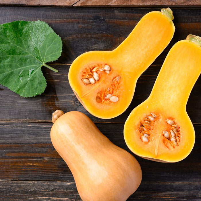 Fresh butternut squash halves with leaf on rustic wood.