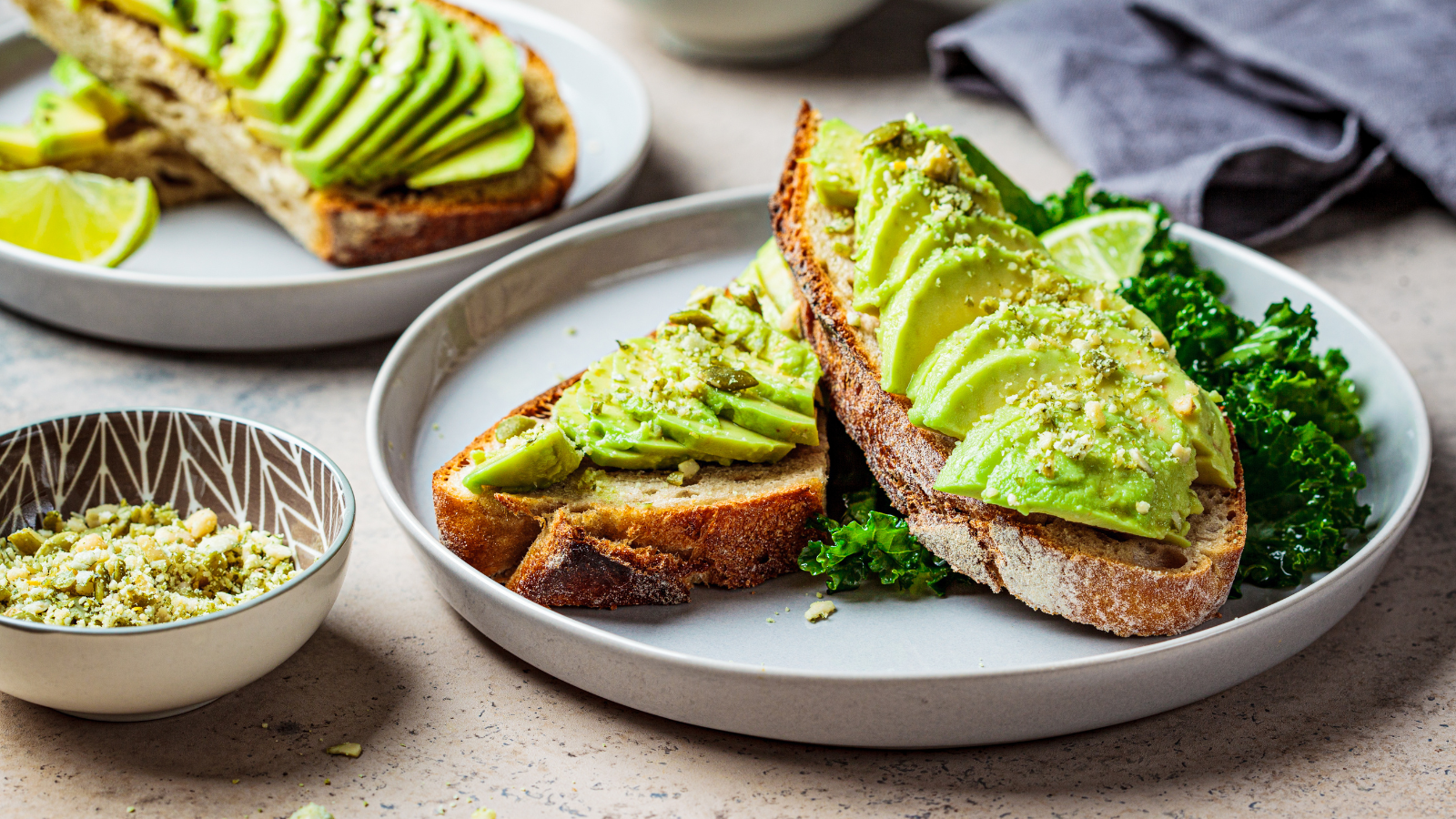 Avocado toast with sliced avocado and kale served on sourdough bread.