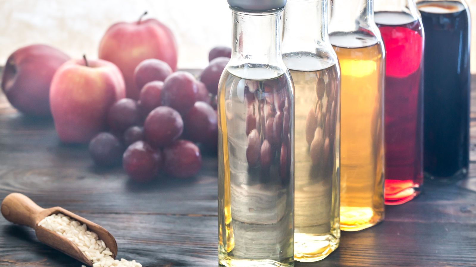 Assorted vinegar bottles with apples and grapes in background.