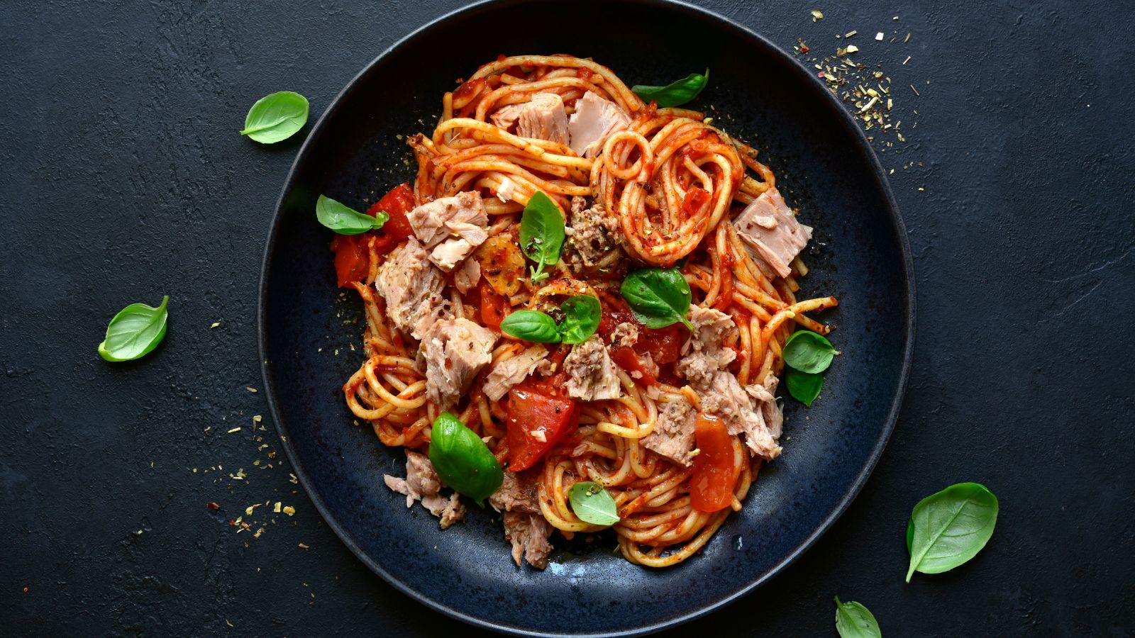 Black plate with spaghetti tuna, veggie pasta sauce, and fresh basil leaves
