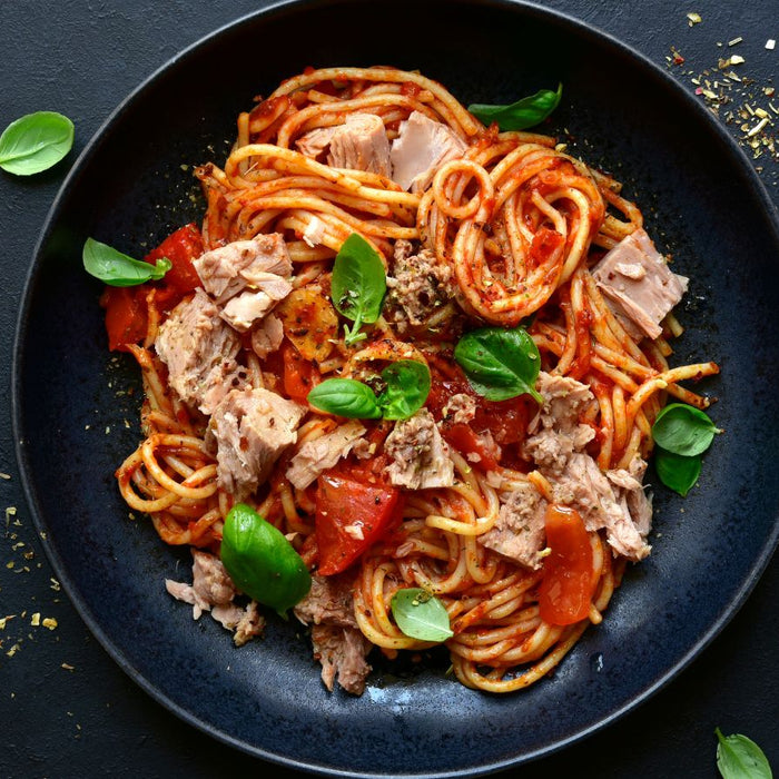 Black plate with spaghetti tuna, veggie pasta sauce, and fresh basil leaves