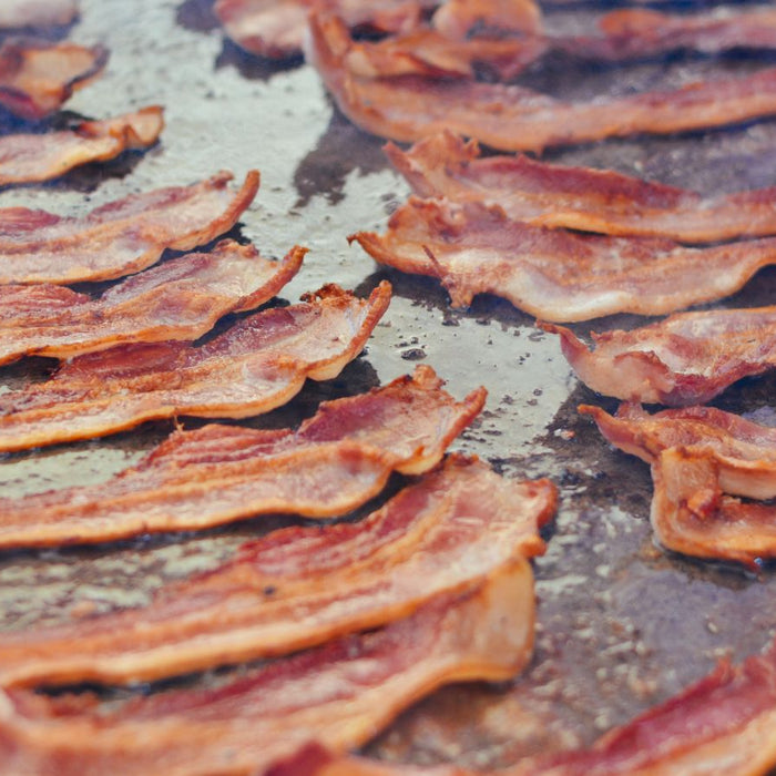 Strips of crispy bacon cooking on a large griddle surface.