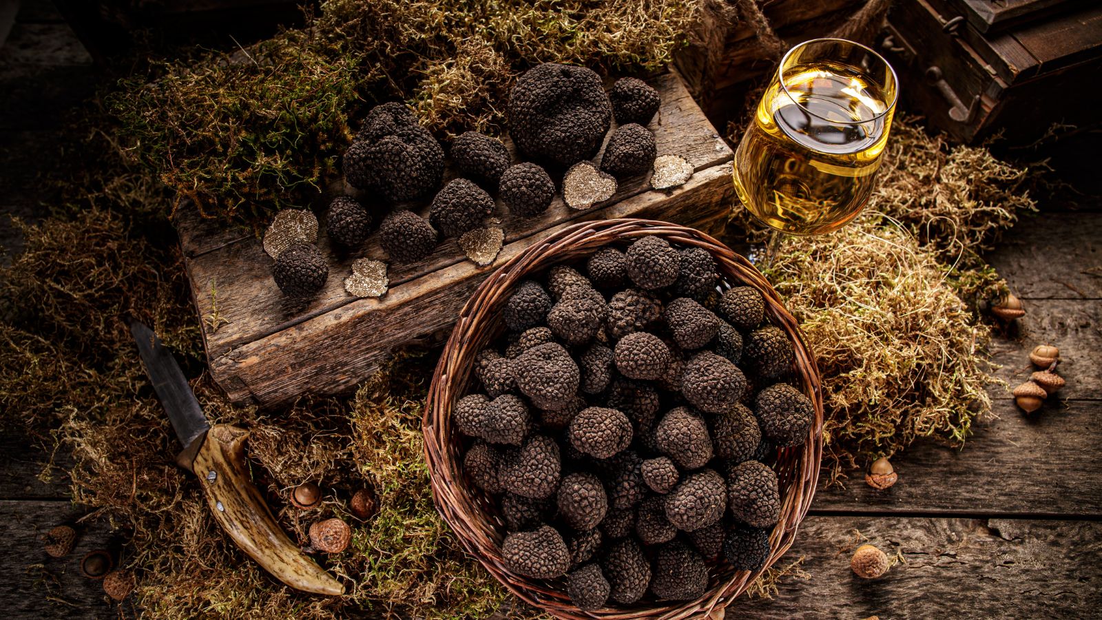 Assorted black truffles in basket and on board with wine glass.