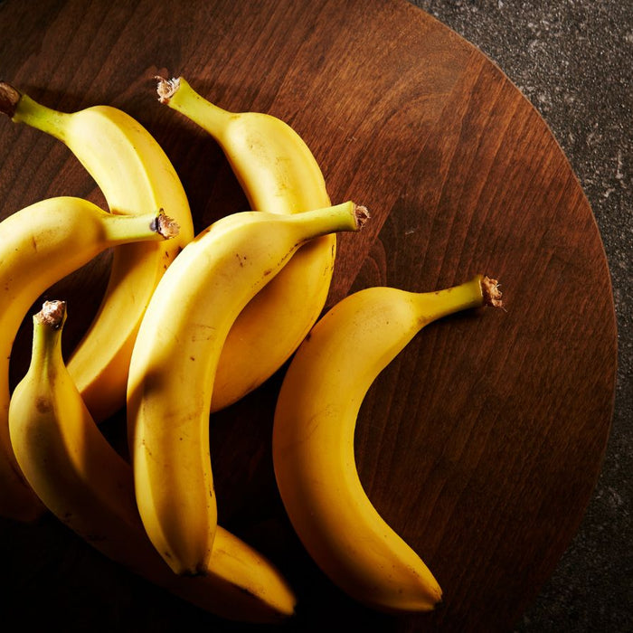 Six ripe bananas laid on a round wooden board over dark surface.