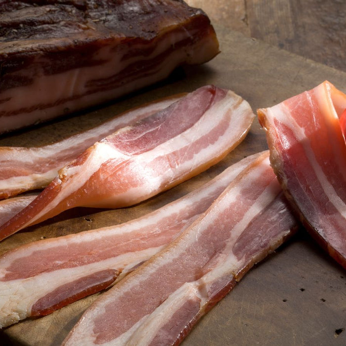 Uncooked bacon slices and slab on rustic wooden cutting board.