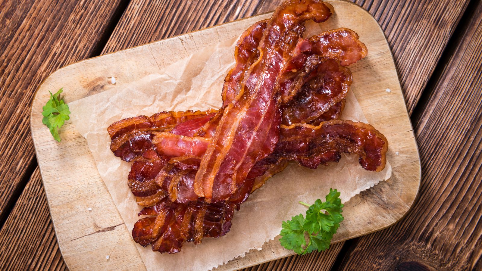 Crispy cooked uncured bacon slices on parchment paper over a wooden board.