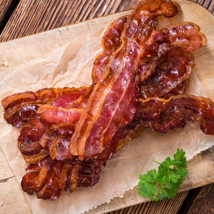 Crispy cooked uncured bacon slices on parchment paper over a wooden board.
