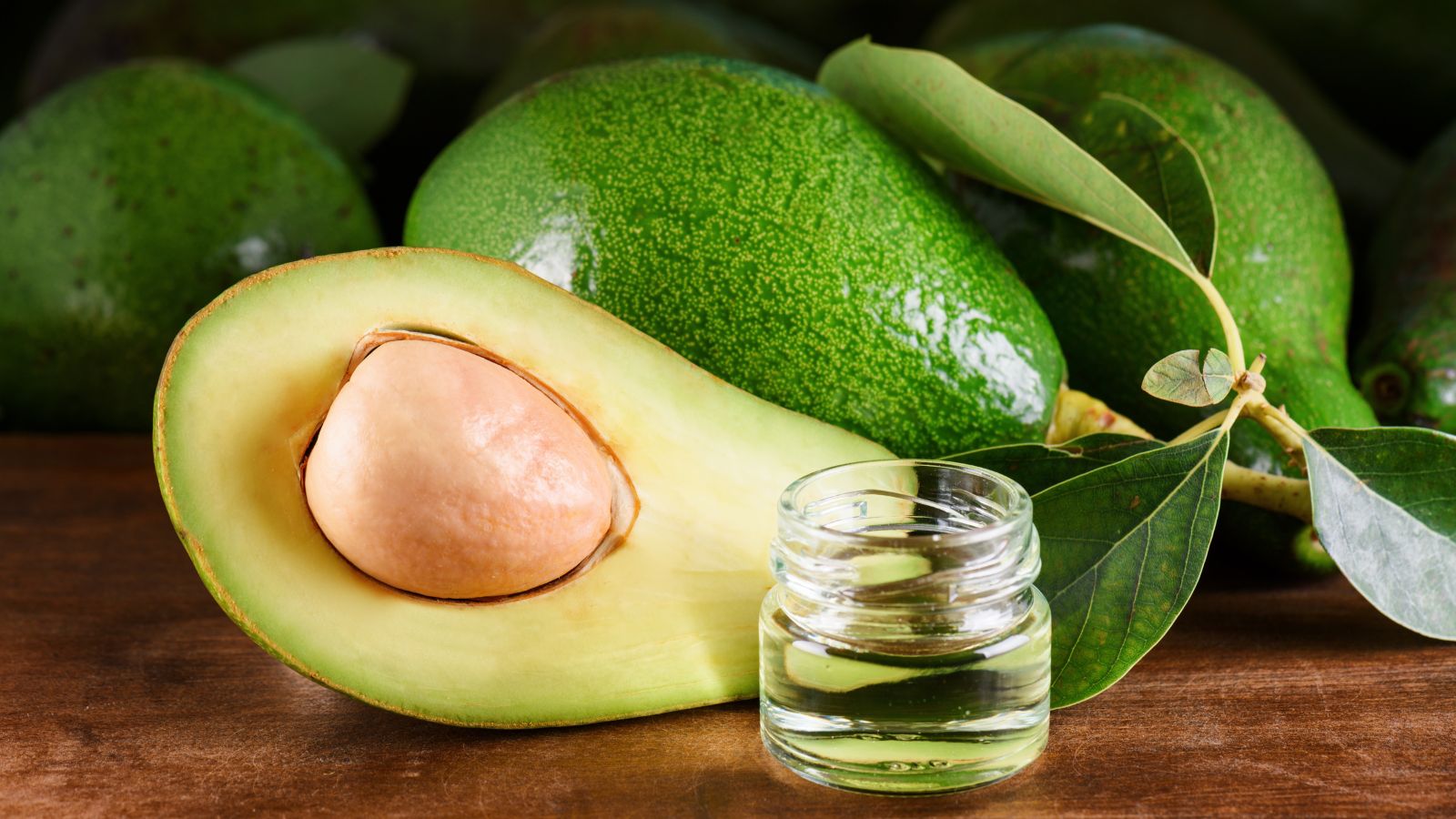 Fresh avocado with small glass jar of avocado oil on a wooden table.