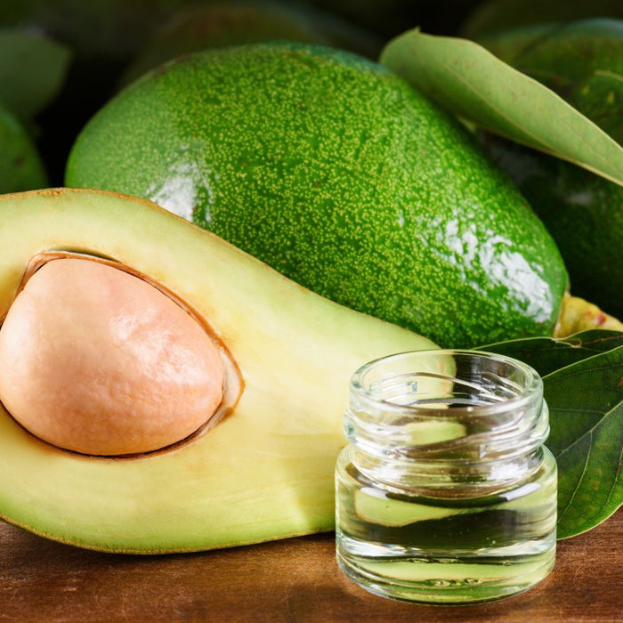 Fresh avocado with small glass jar of avocado oil on a wooden table.