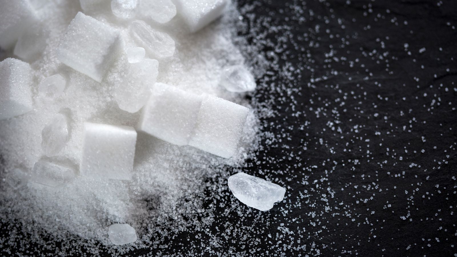 Close-up of sugar cubes and crystals scattered on black surface.