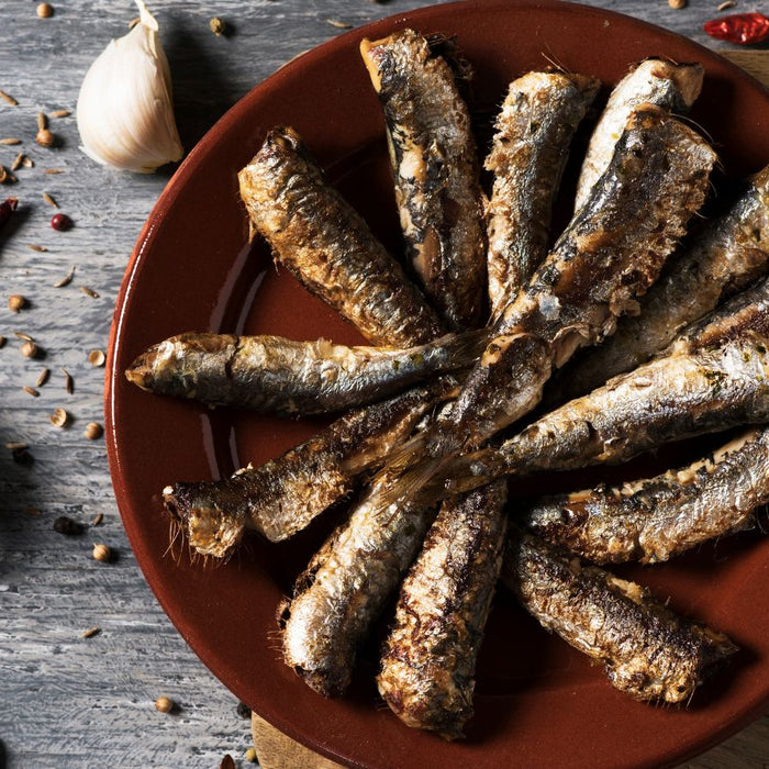 Grilled sardines on a plate with garlic, lemon, and spices.