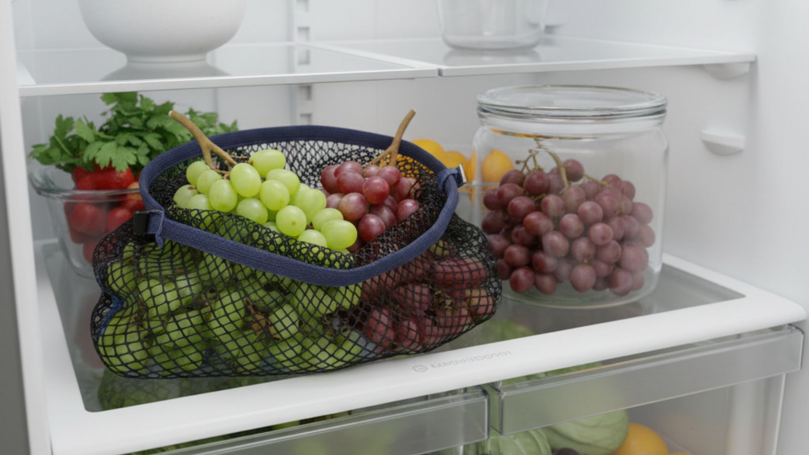 Mesh bag of green and red grapes stored on refrigerator shelf