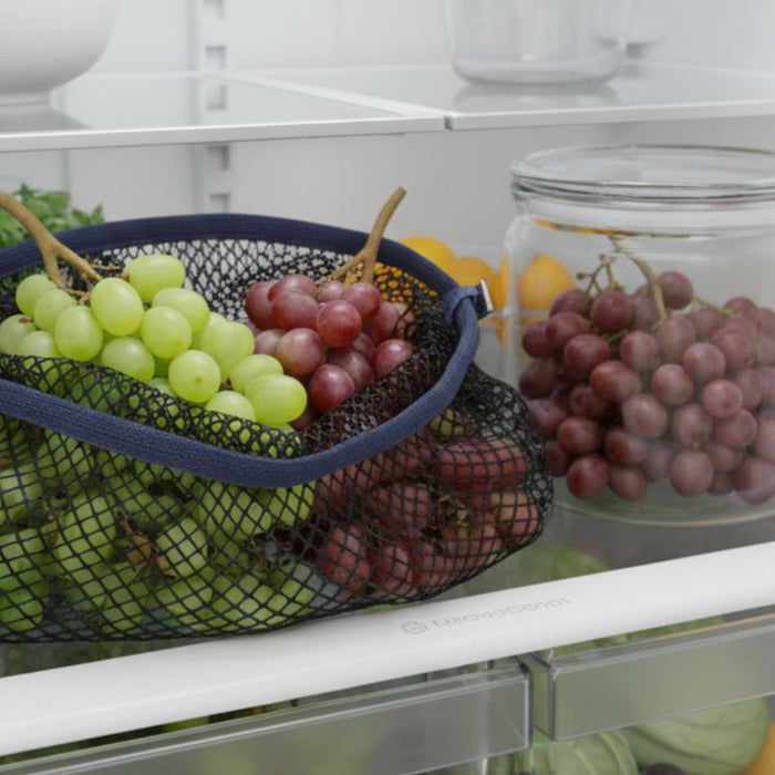 Mesh bag of green and red grapes stored on refrigerator shelf