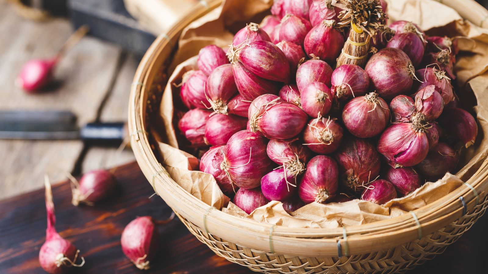 Fresh purple onions in a woven basket on wooden table