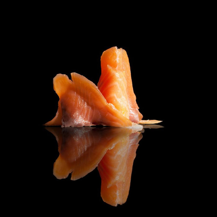 Thin slices of smoked salmon with reflection on black surface.