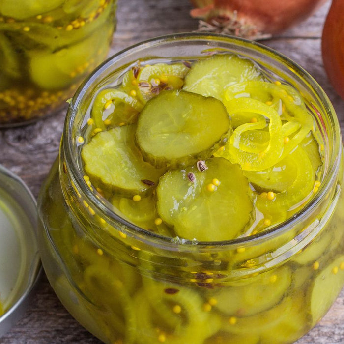 Open jar of sliced dill pickles resting on a rustic wooden table.