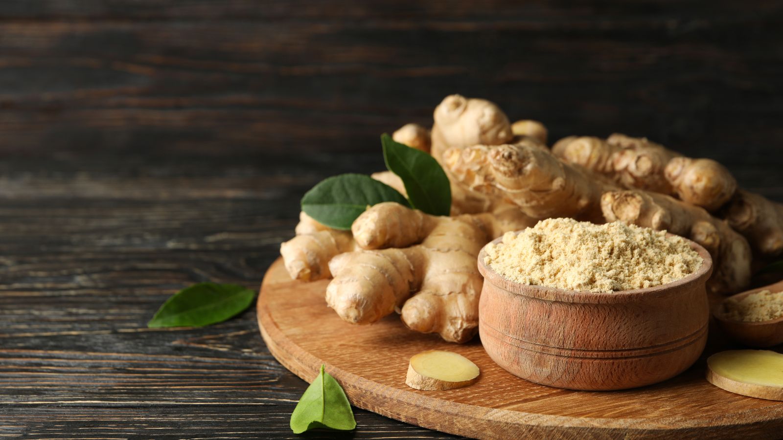 Ground ginger powder in wooden bowl with fresh ginger roots