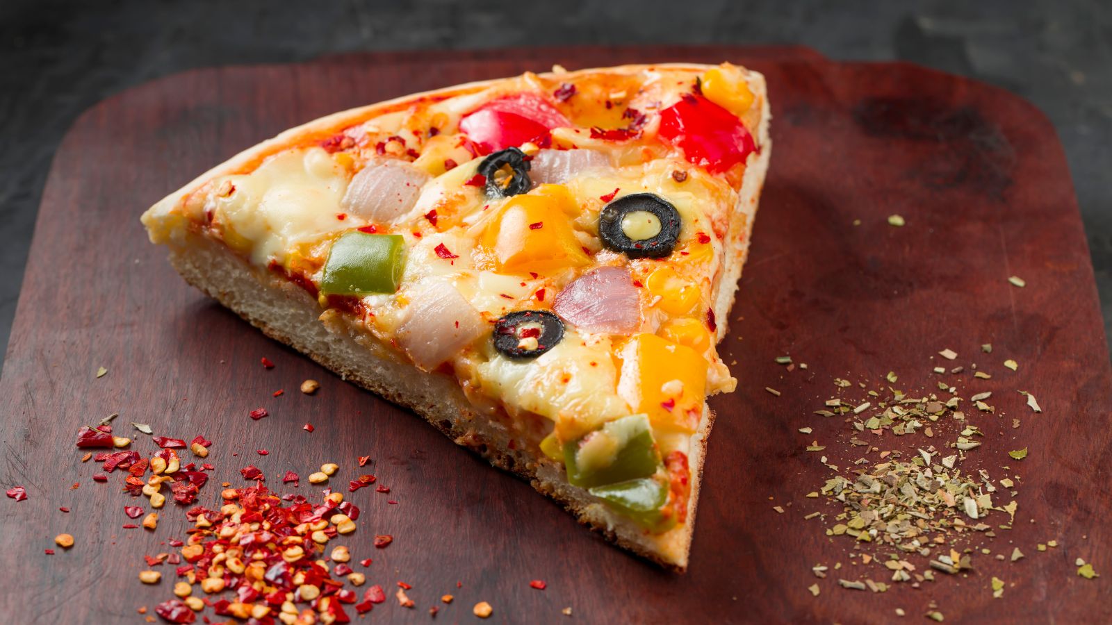 Slice of veggie pizza with toppings on wooden board.