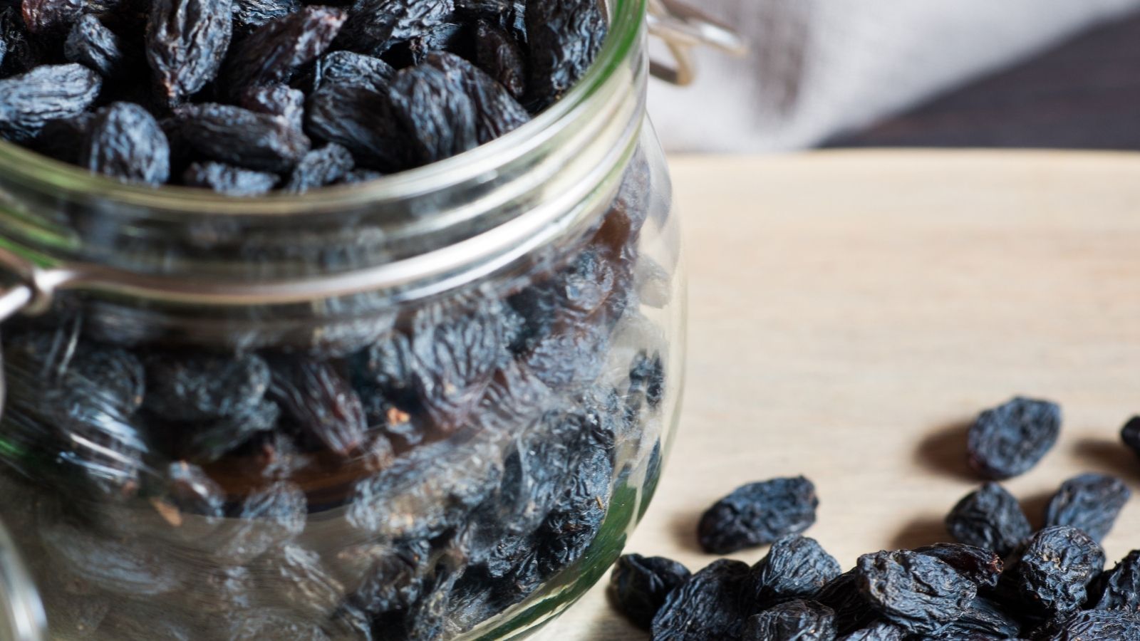 Glass jar filled with black raisins spilling onto a wooden surface.
