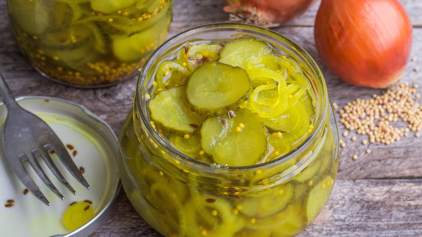 Open jar of sliced dill pickles resting on a rustic wooden table.