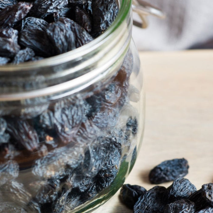 Glass jar filled with black raisins spilling onto a wooden surface.