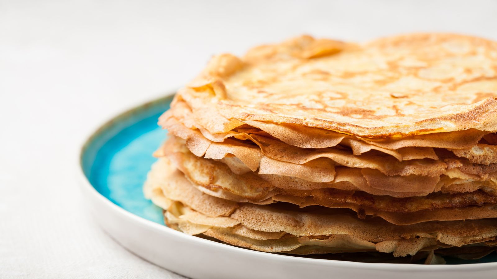 Stack of golden brown crepes on a blue plate ready to be served