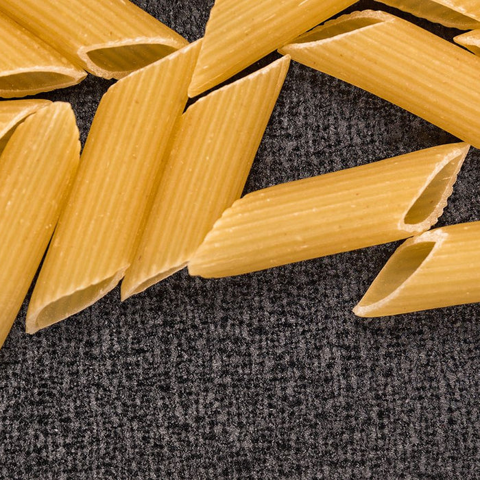 Close-up of uncooked penne pasta scattered on dark textured surface