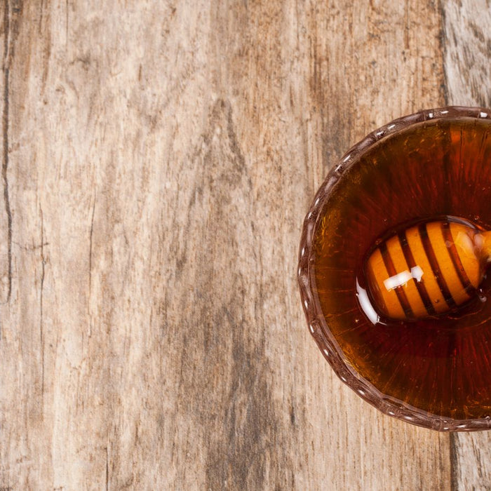 Bowl of golden honey with wooden dipper on rustic wooden table
