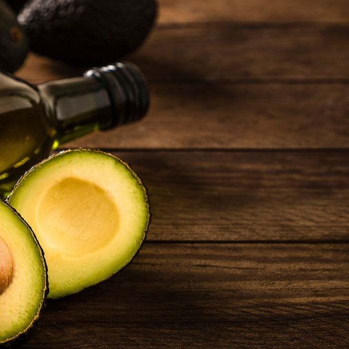 Avocado cut in half beside bottle of avocado oil on rustic wooden table