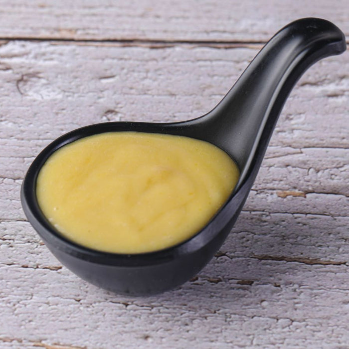 Spoonful of yellow mustard on rustic light wooden background.