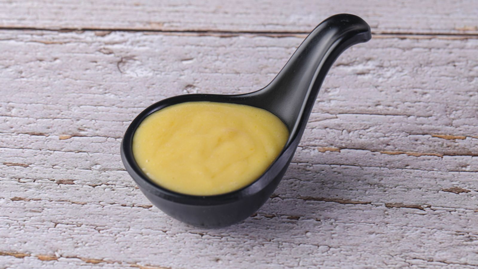 Spoonful of yellow mustard on rustic light wooden background.