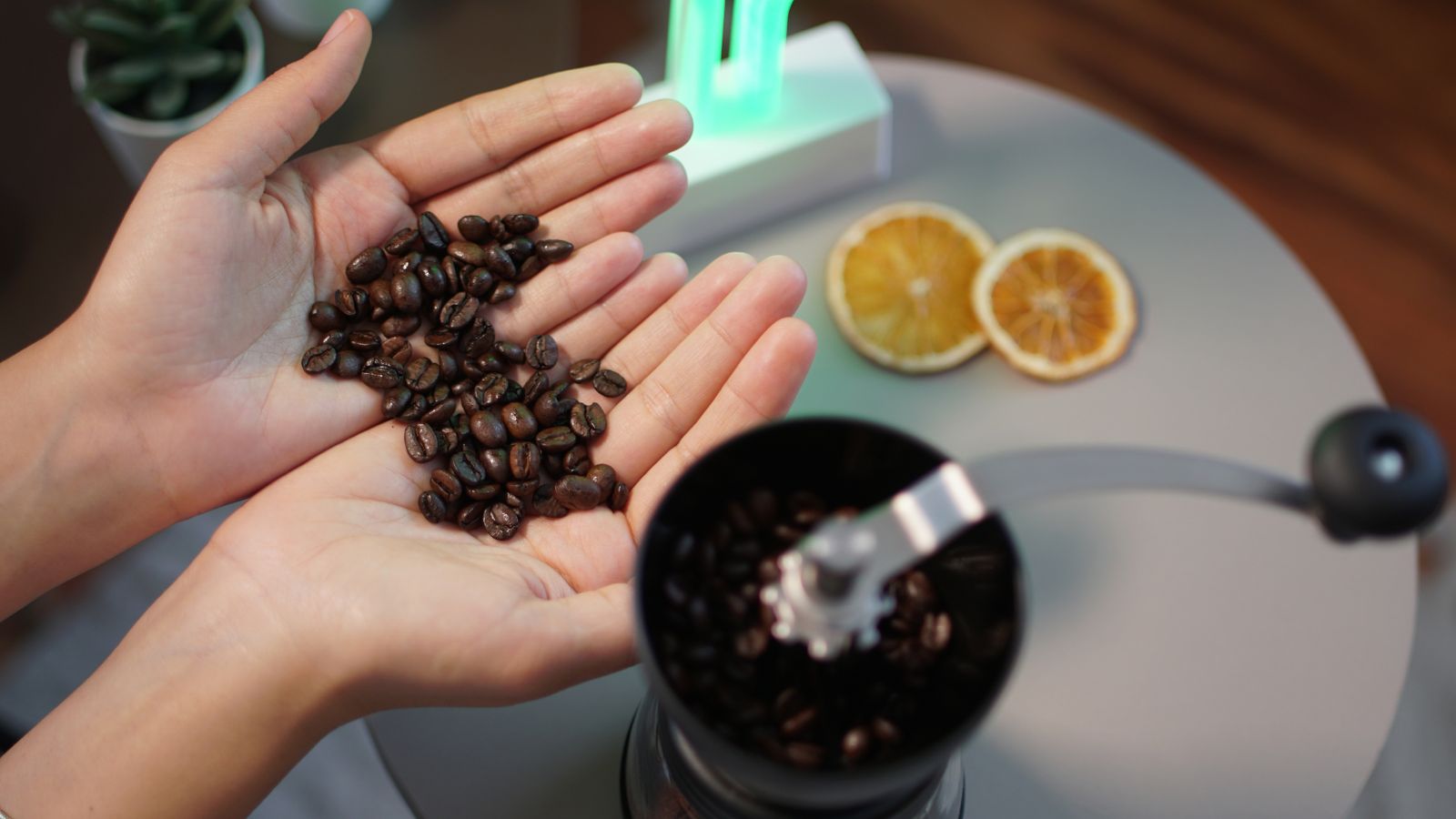 Hands holding coffee beans above a manual coffee grinder.