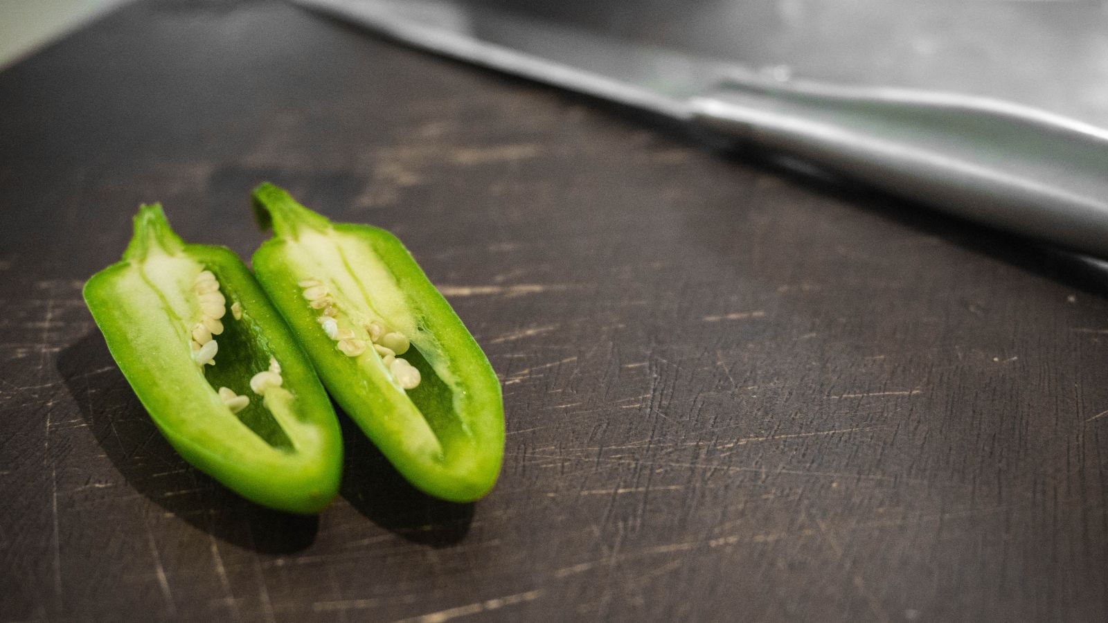 Sliced jalapeño halves on dark cutting board beside knife
