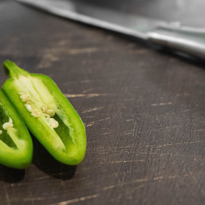 Sliced jalapeño halves on dark cutting board beside knife