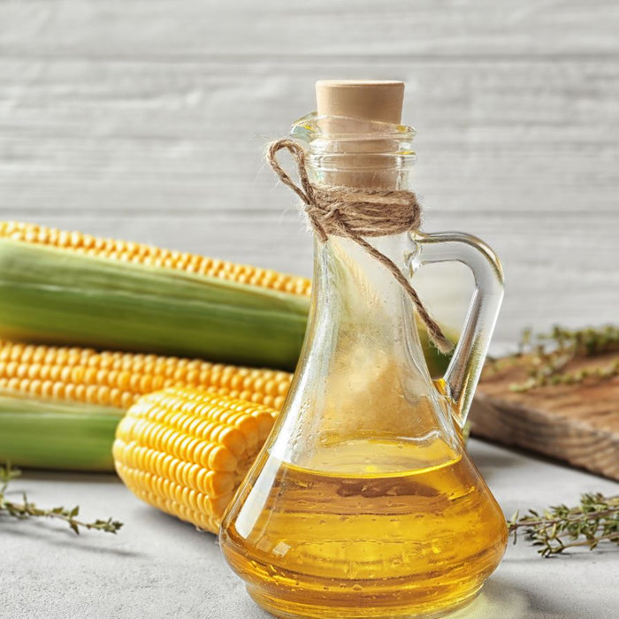 Vegetable oil in glass jar with fresh corn and herbs on table.