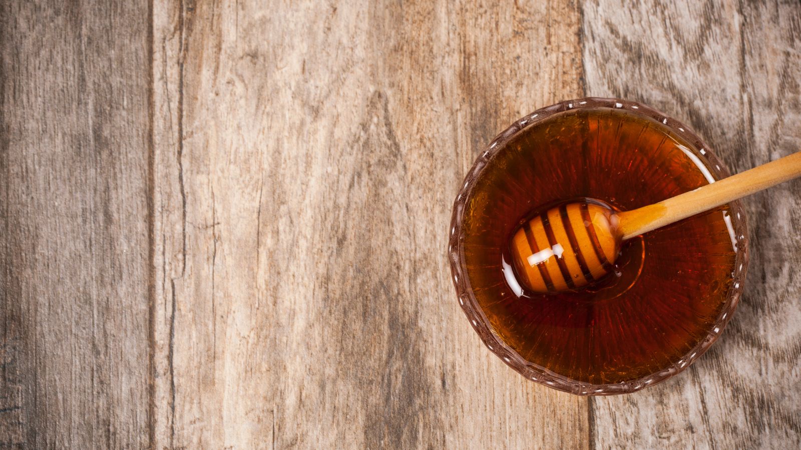 Bowl of golden honey with wooden dipper on rustic wooden table