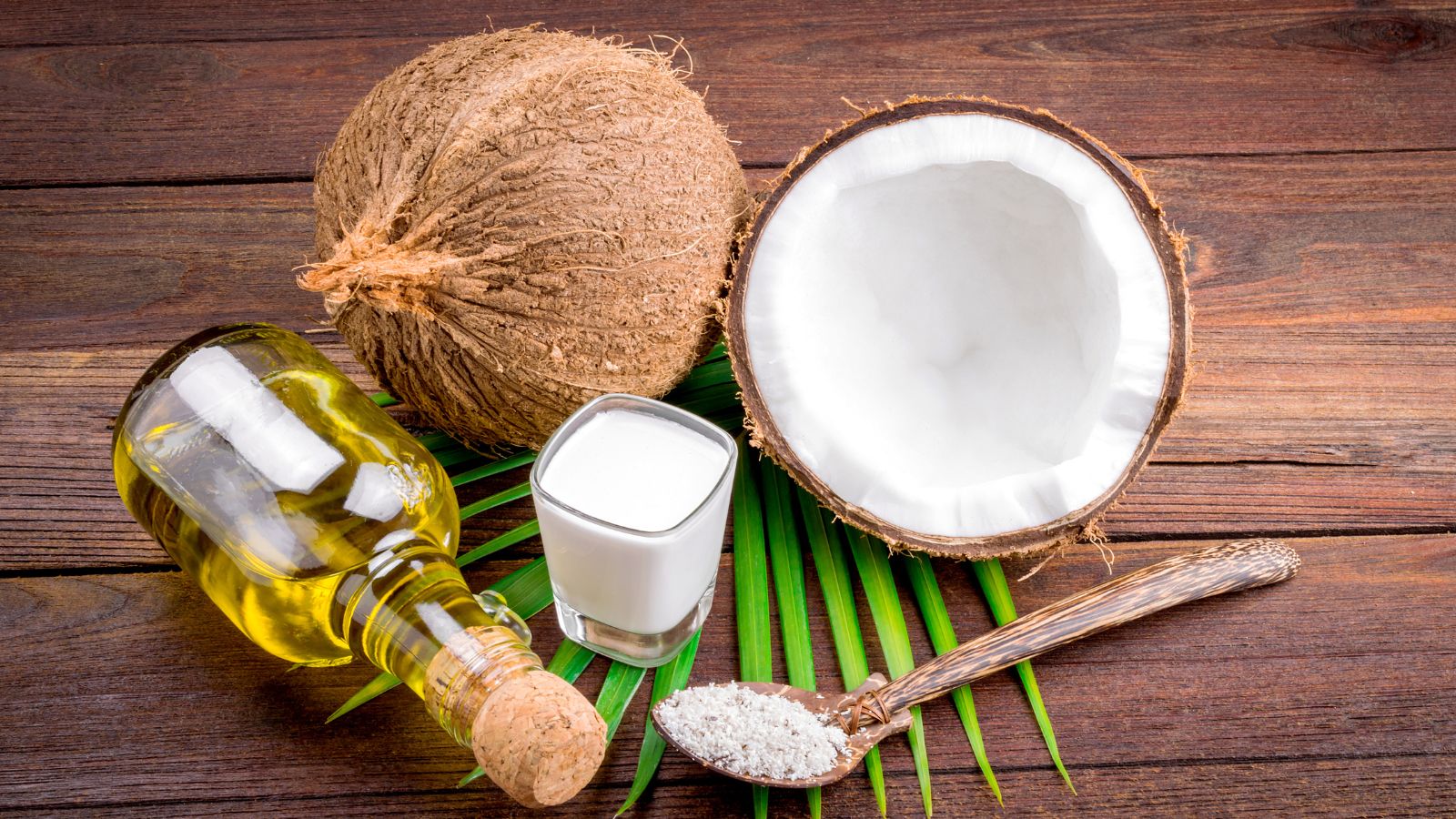 Coconut, coconut oil, and milk arranged on a wooden surface.