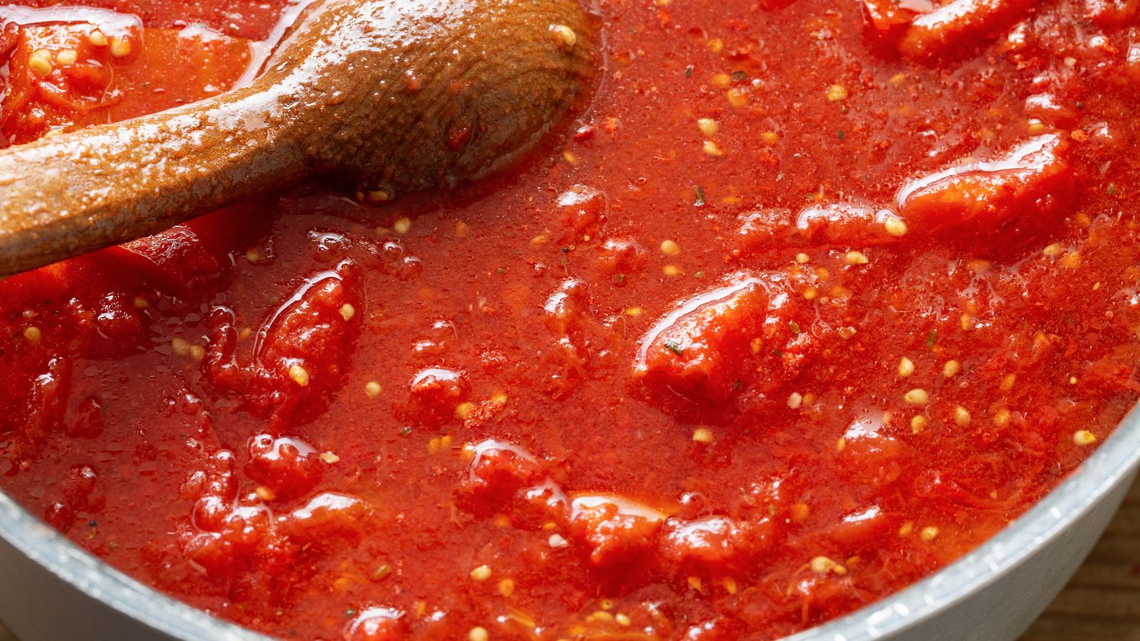 Tomato sauce with seeds and chunks being stirred in a pan.