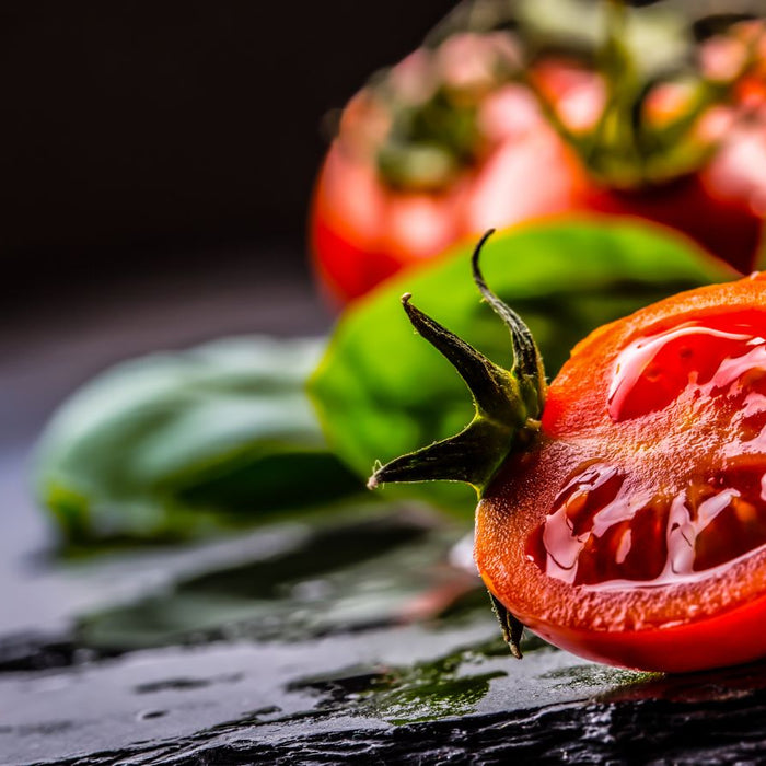 Fresh sliced tomatoes with basil leaves on a dark background.