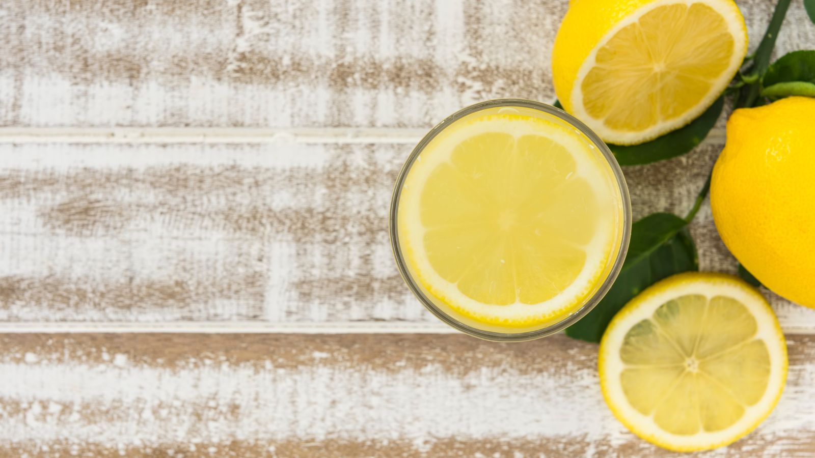 Glass of lemonade with lemon slices and whole lemons on rustic table