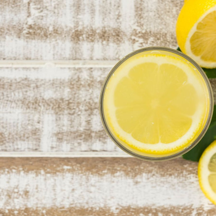 Glass of lemonade with lemon slices and whole lemons on rustic table
