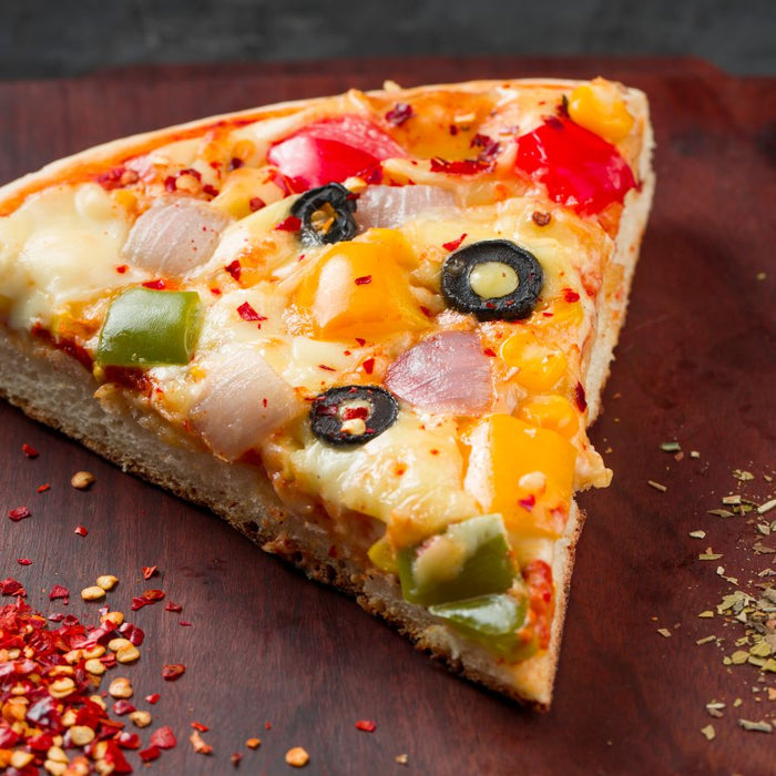 Slice of veggie pizza with toppings on wooden board.