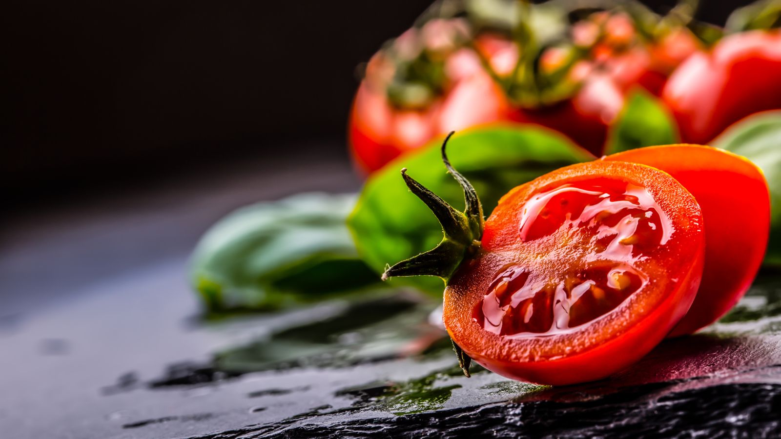 Fresh sliced tomatoes with basil leaves on a dark background.