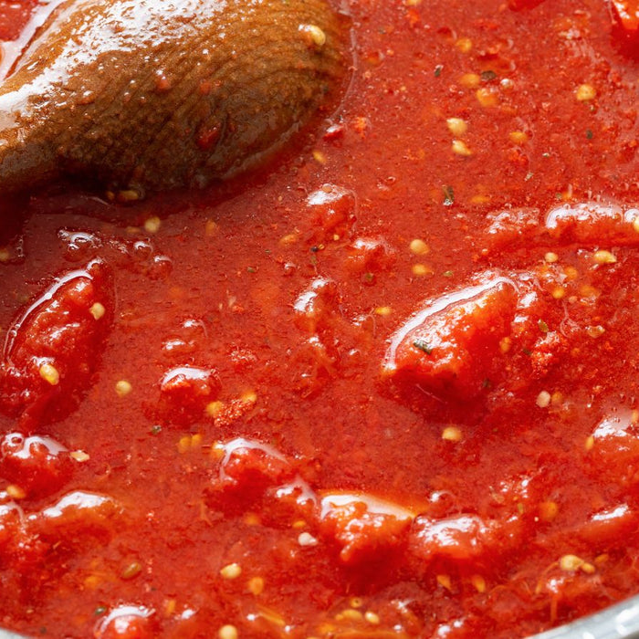 Tomato sauce with seeds and chunks being stirred in a pan.