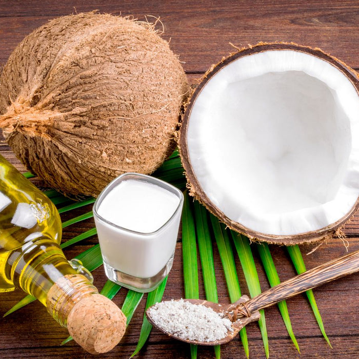 Coconut, coconut oil, and milk arranged on a wooden surface.